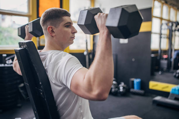 istock Man seated for dumbbell presses, strong and focused 2176474625