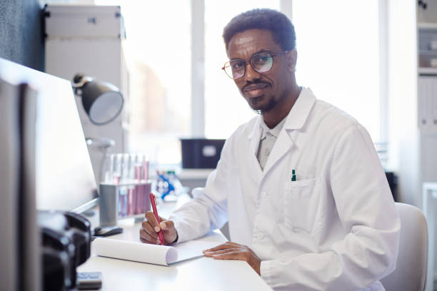 istock Portrait of Male Chemist Smiling while Writing at Working Table in Laboratory 2176475724