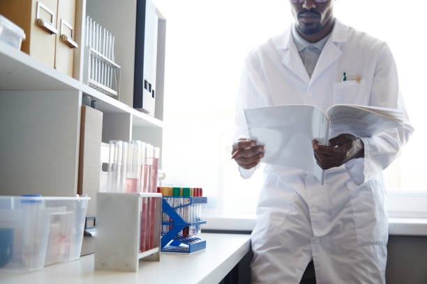 istock Male Lab Chemist Reading Book next to Window in Pharmaceutical Laboratory 2176475732