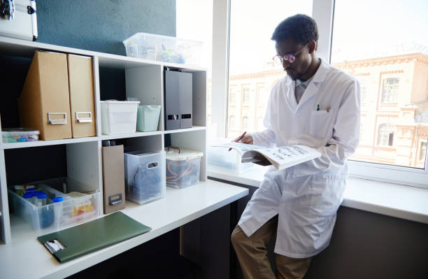 istock Male Scientist Reading Book while Standing next to Cabinet in Laboratory 2176475733