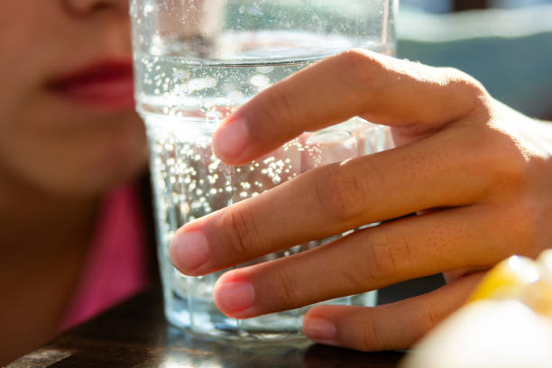 A child's hand holds a glass with sparkling water on the table