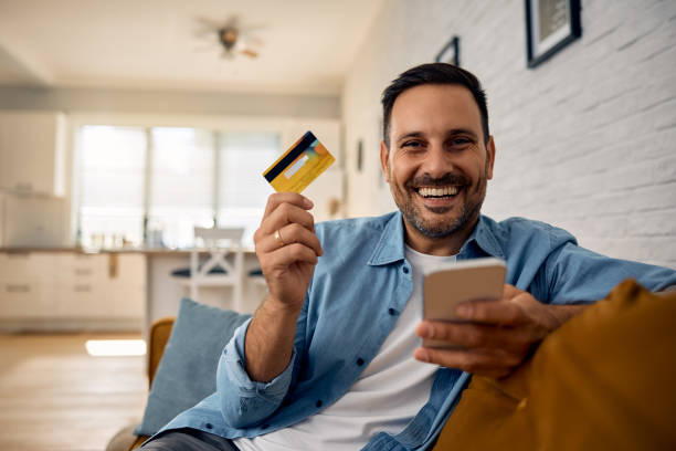 istock Happy man using credit card and mobile phone while banking online and looking at camera. 2176488555
