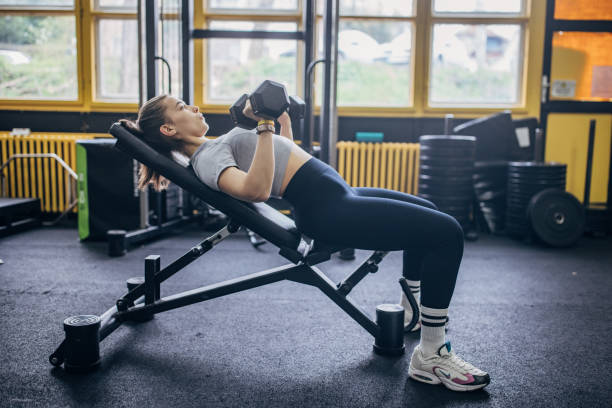 Athletic woman lifting weights on incline gym bench