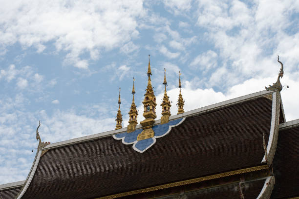 Traditional rooftop design featuring five pagodas at the center with a blue sky and clouds. Wat Rajamontean in Chiang Mai, Thailand.