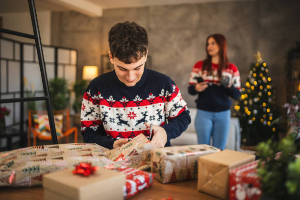 istock young man wrap Christmas gift with festive decorations at home 2176508701