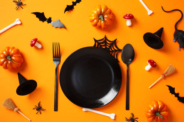 istock Halloween table setting with pumpkins, bats, spiders, witch hats, and spooky decorations on orange background. 2176513334