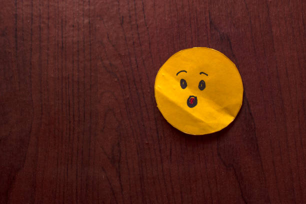 Close-up of a surprise face emoji placed on a rustic wooden background. Perfect for concepts related to shock, surprise, or expression in social media or communication designs.