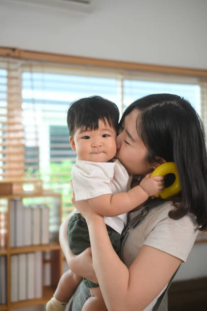 Loving young mother holding her cute baby boy and lovingly kissing on his cheek Loving young mother holding her cute baby boy and lovingly kissing on his cheek. baby boy dancing with his mommy stock pictures, royalty-free photos & images