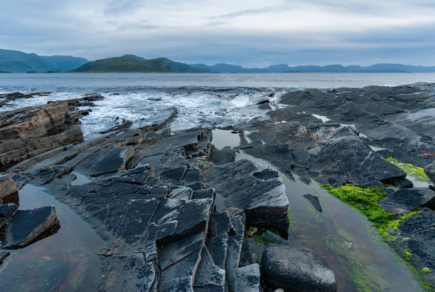 istock Vast rocky shoreline at twilight, reflecting calm waters and distant hills under a cloudy sky 2176598031