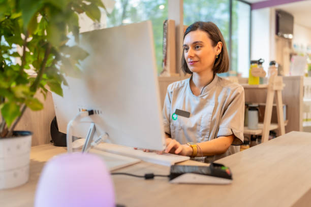 istock Young pharmacist using computer sitting in the counter of store 2176603196