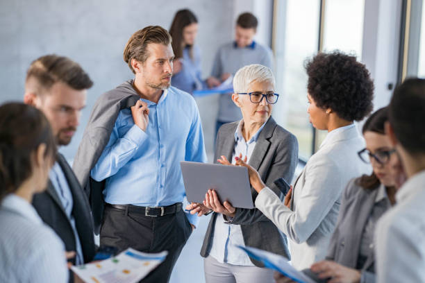 istock Business colleagues talking while using laptop in a hallway full of people. 2176603995