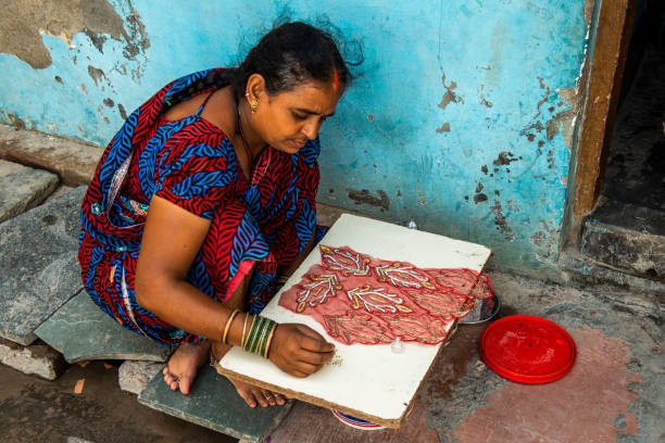 New Delhi, India-September 22, 2015: A woman creates an intricate design on a piece of cloth in her decrepit house, showcasing her artistry and resilience.