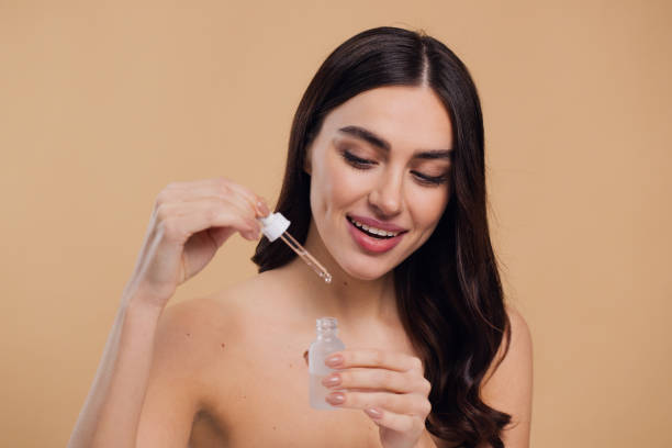 istock Woman Dropping Serum on Face on Beige Background 2176612947