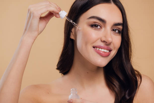 istock Woman Dropping Serum on Face on Beige Background 2176613167