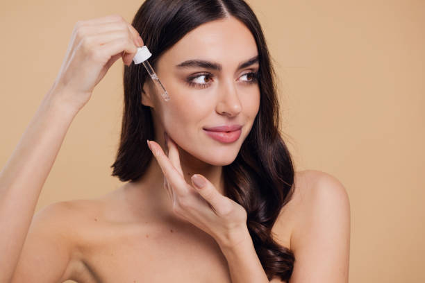 istock Woman Dropping Serum on Face on Beige Background 2176619117