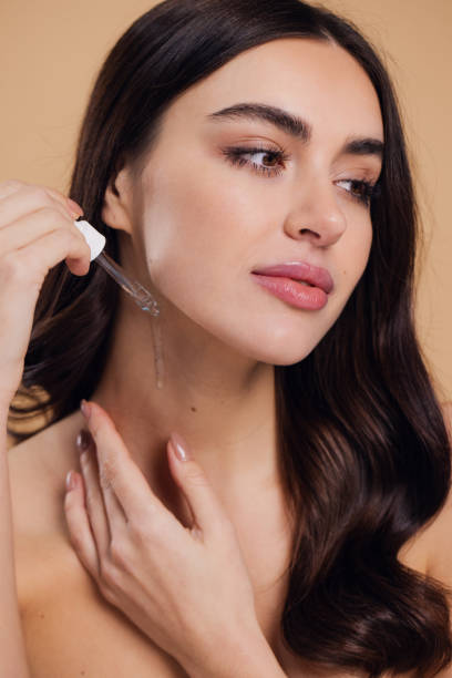 istock Woman Dropping Serum on Face on Beige Background 2176621328