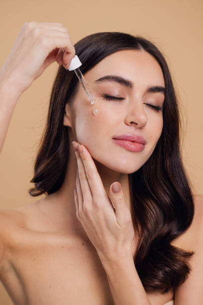 istock Woman Dropping Serum on Face on Beige Background 2176621331