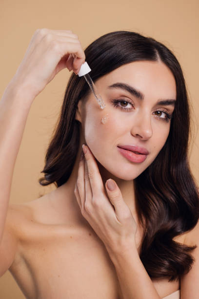 istock Woman Dropping Serum on Face on Beige Background 2176622665