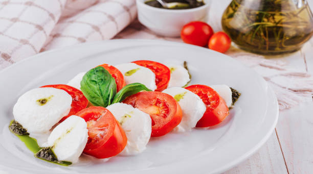istock Caprese salad with tomatoes, mozzarella cheese, pesto and basil on white plate 2176625609