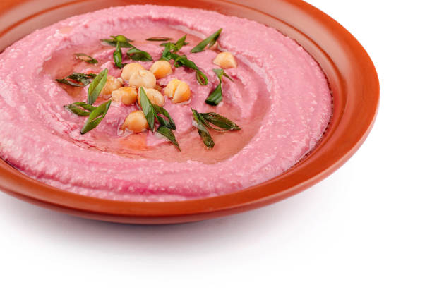 Pink beetroot hummus decorated with chickpeas and green onions, served on a clay dish, isolated on white background
