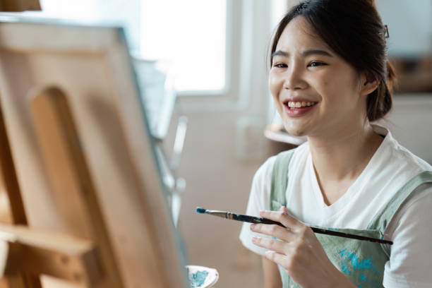 istock Young Female Artist Smiling While Painting on Canvas in Bright Studio 2176626620