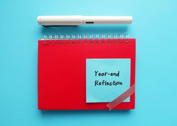 Red notebook with handwritten text note YEAR-END REFLECTION - best end-of-year rituals to reflect or review success, failures or and lessons learnt from past year and plan for the next coming year