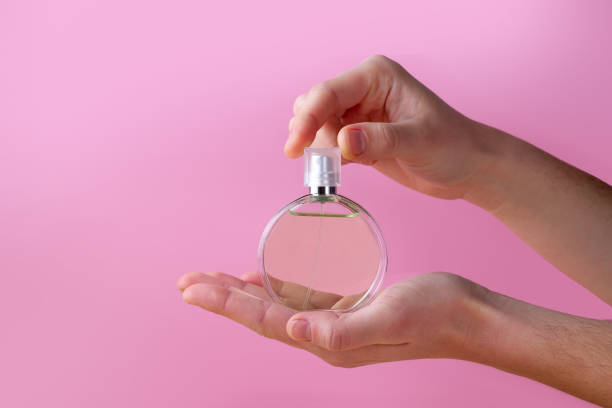 istock Bottle of women's perfume in hands on a pink background. 2176628651