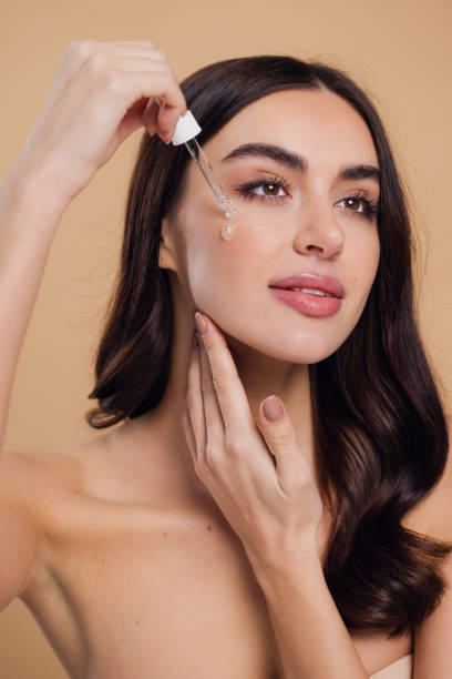 istock Woman Dropping Serum on Face on Beige Background 2176628753