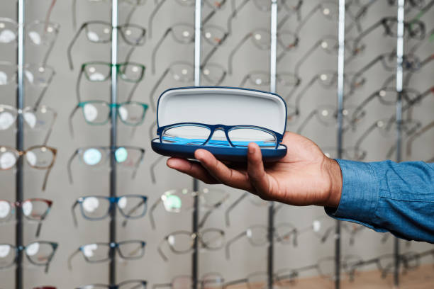Optometrist Holding Eyeglasses in Store with Spectacles Display in Background