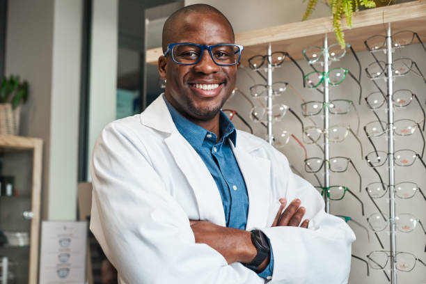 istock Confident Optometrist in White Coat Smiling in Eyewear Store with Display of Spectacles 2176634964