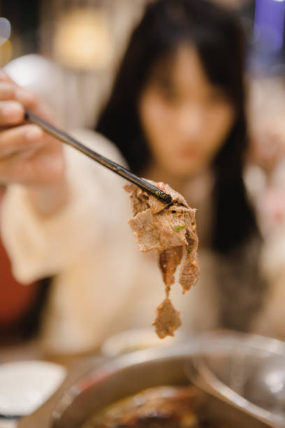 An Asian woman is eating beef hotpot at a restaurant, displaying cooked beef