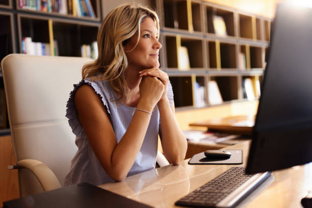 Smiling businesswoman day dreaming while working on PC in the office.
