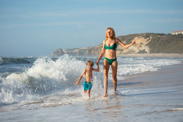 istock Woman and young boy having fun in ocean waves at a sandy beach 2176657717
