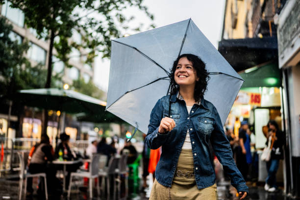 istock Young woman using umbrella and walking through the city 2176660547