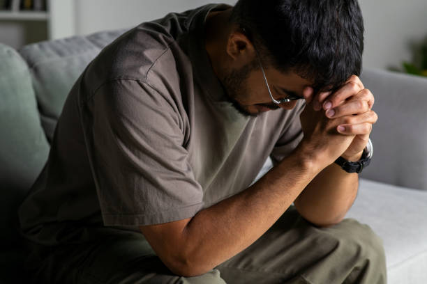 istock Young Asian man sitting on a sofa at home, looking sad and exhausted, struggling with depression and mental health issues. 2176663714