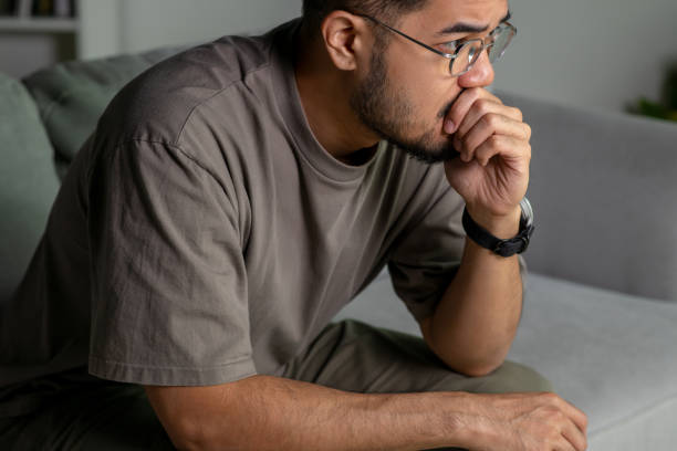 istock Young Asian man sitting on a sofa at home, looking sad and exhausted, struggling with depression and mental health issues. 2176663736