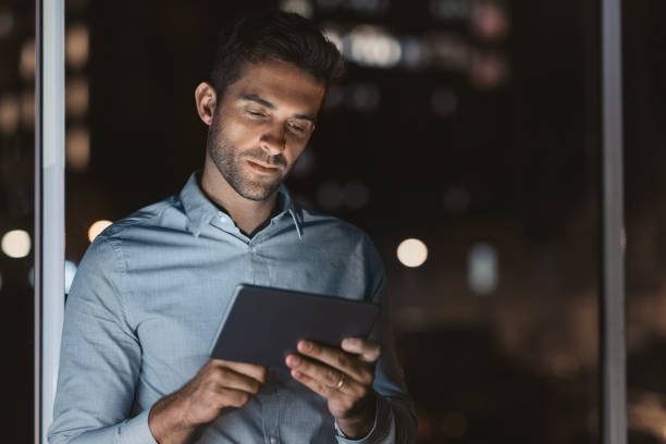 istock Handsome businessman using a tablet in his office at night 2176664326
