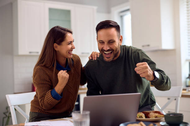 istock Happy couple celebrating good news while using laptop in the kitchen. 2176665994