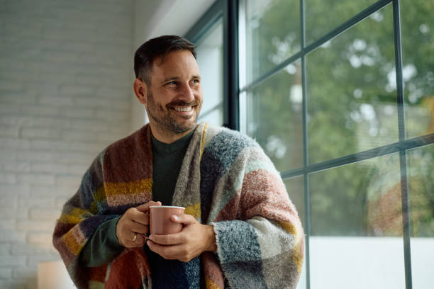 istock Happy man wrapped in blanket enjoying in view from his window. 2176666219