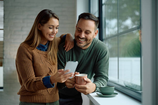 istock Happy couple using mobile phone while relaxing by the window at home. 2176666366