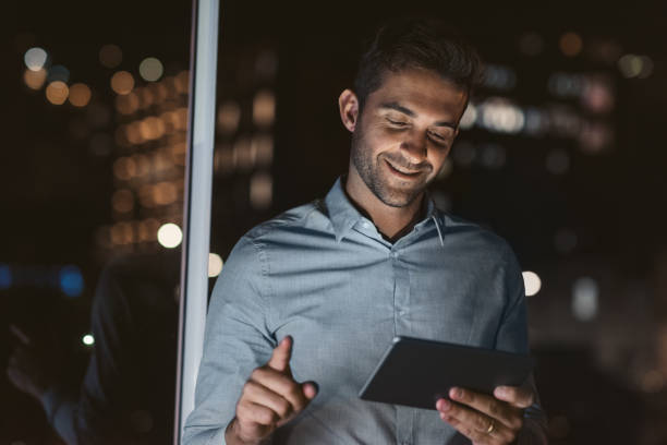 istock Smiling businessman standing in his dark office using a tablet 2176666974