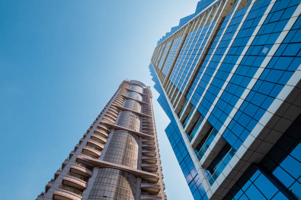 This stock photo showcases a modern architecture building, a tall skyscraper converging into the sky, representing a commercial hub. The sleek lines and towering structure reflect the sophistication and corporate environment of the city’s business sector. Ideal for projects related to urban development, corporate architecture, and commercial real estate.