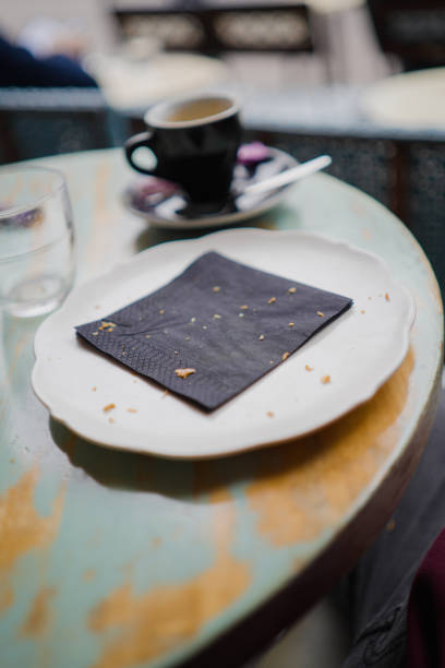 Empty White Plate with a Black Napkin and Crumbles After Breakfast on a Wooden Round Table