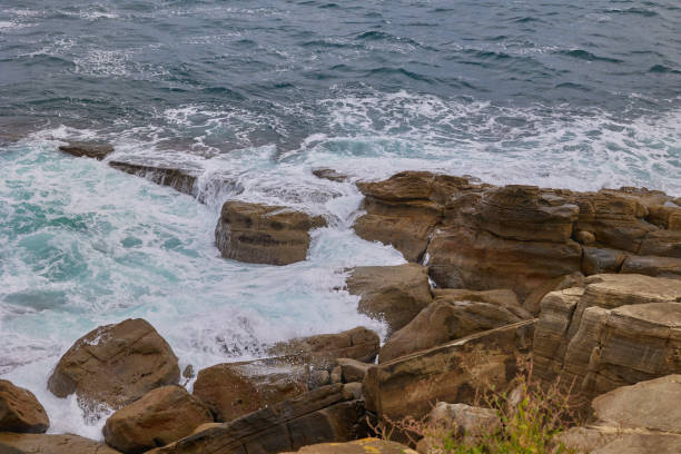 A sea wave rolls onto coastal rocks.