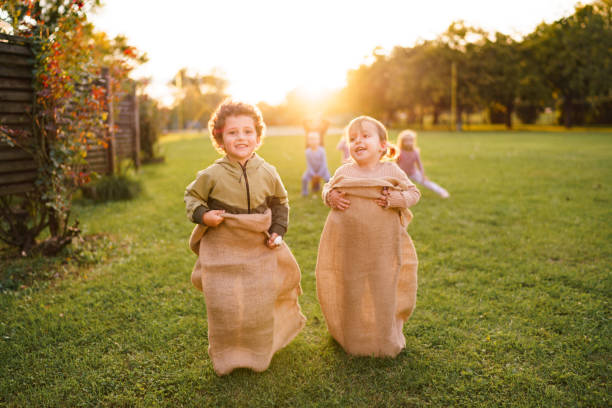 Group of happy little children having fun in sack race outdoors