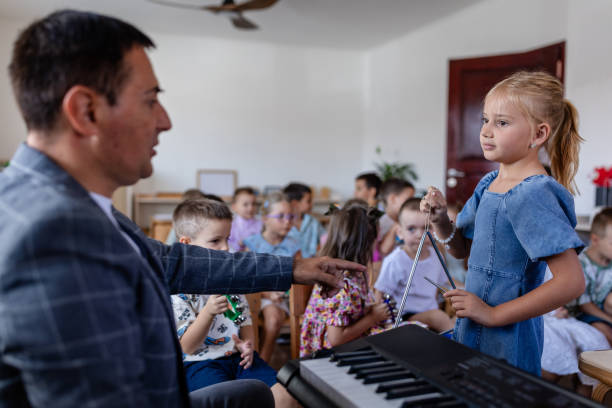 istock Girl plays triangle as teacher points in classroom. 2176687276