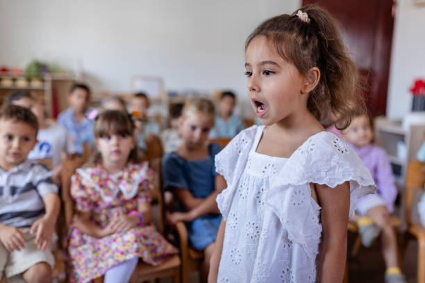 A passionate girl dressed in white is singing during a school performance event, capturing the attention and admiration of her seated classmates.
