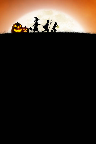 Children trick or treating and two jack o'lanterns are silhouetted by a rising full moon on Halloween night.