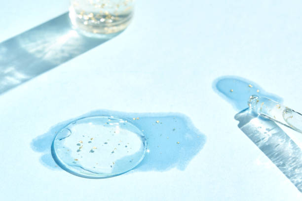 istock Serum gel texture swatch. Transparent drop with golden sparkles. Blue background 2176693170