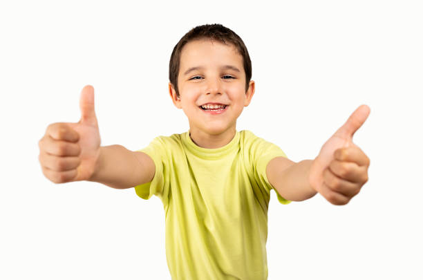 Studio shot of a child wearing casual yellow t-shirt over white background success sign doing positive gesture with hand, thumbs up smiling and happy. Cheerful expression and winner